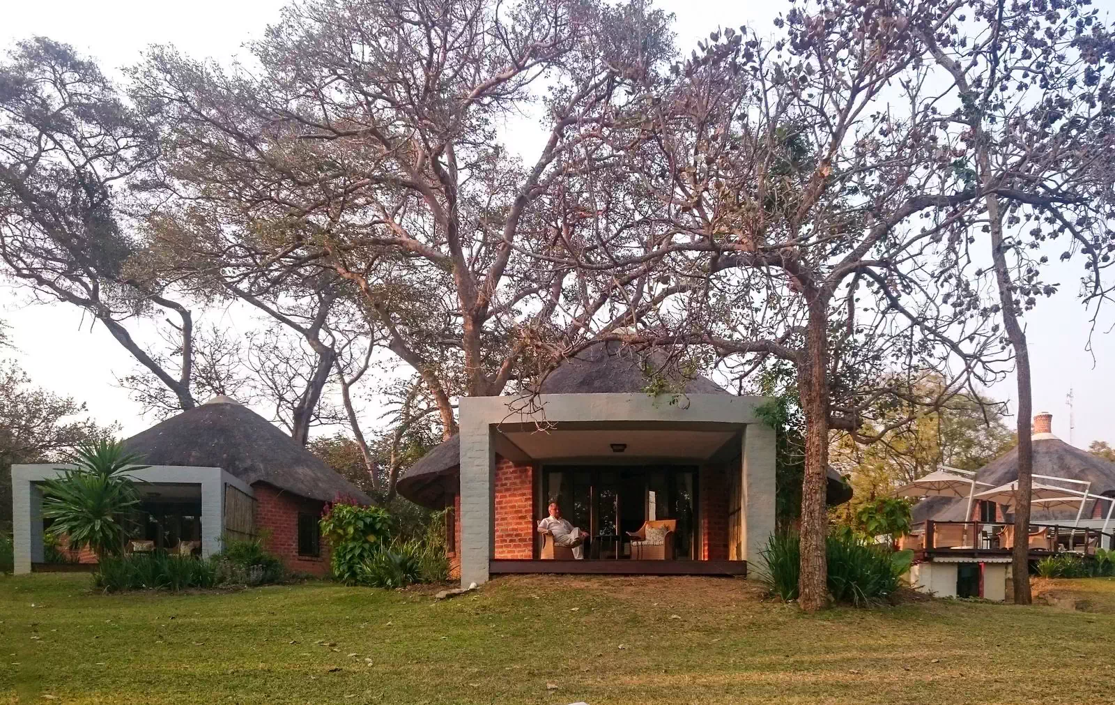 Modern thatched bungalow with covered veranda overlooking lawn and trees behind