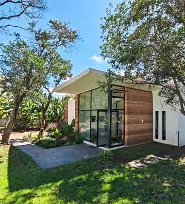 Modern glass entrance to rammed earth building with large cantileavered overhang providing shade