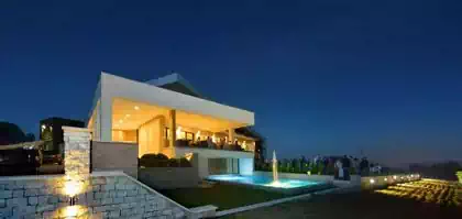 Illuminated night view of pool in front of balcony and entrance to modern spectacular building
