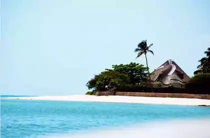 Blue ocean, white sand, palm tree and thatched roof bungalow on Magaruque Island, Vilankulos