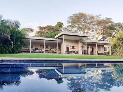 Pool overlooking modern Harare house with horizontal overhanging roof supported by steel columns. Design by architect from Harare