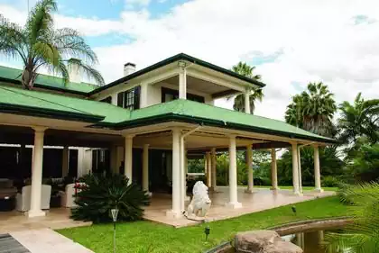 Imposing veranda with round columns and two stories. Palm trees integrated into design and heavily shaded veranded in vegitation