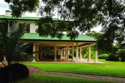 Imposing veranda with round columns and two stories. Palm trees integrated into design and heavily shaded veranded in vegitation
