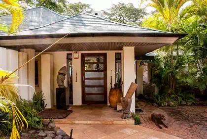 Elegant covered entrance with african sculptures and double slopped shingled roof immersed in vegetation in Mazowe